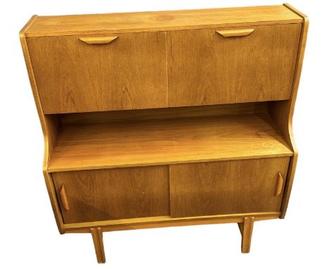 A teak mid century drinks cabinet, with two fall front cupboards enclosing fitted interior above pair of sliding cupboard doo