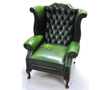 A green leather button upholstered wing back arm chair on squat cabriole front legs.