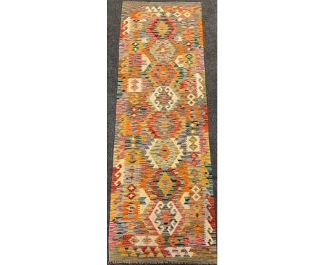 A Turkish Anatolian Kilim runner carpet / rug, knotted in bright tones of red, jade green, yellow, and blue, 253cm x 87cm. 