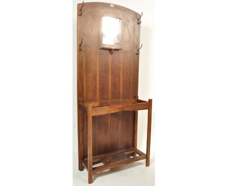 A 1920s Arts and Crafts oak hall stand having a mirror to the centre flanked by cost hooks with glove drawer below and umbrel