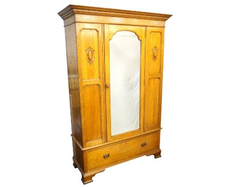 EDWARDIAN OAK MIRROR-DOOR WARDROBE
with shaped cornice, carved panel detail flanking the central mirror, raised on single dra