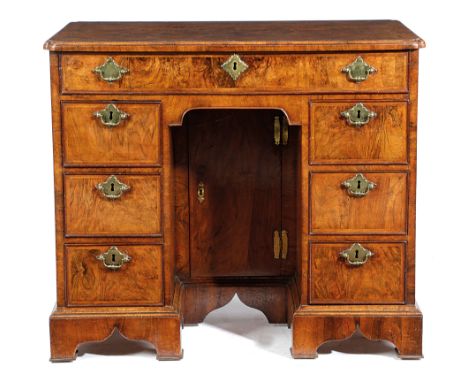 A GEORGE II WALNUT KNEEHOLE DESK C.1725 the quarter veneered top with cross and feather banding and re-entrant corners, with 