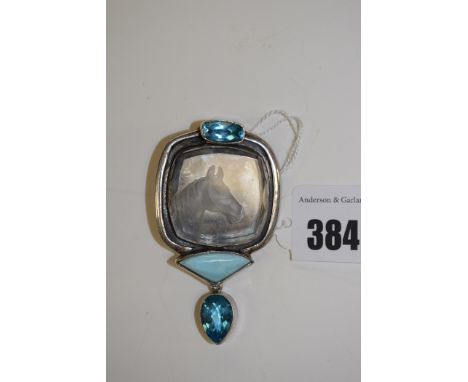 A reverse engraved glass and blue stone brooch/pendant, the glass panel showing a horses head surrounded by blue stones, in w