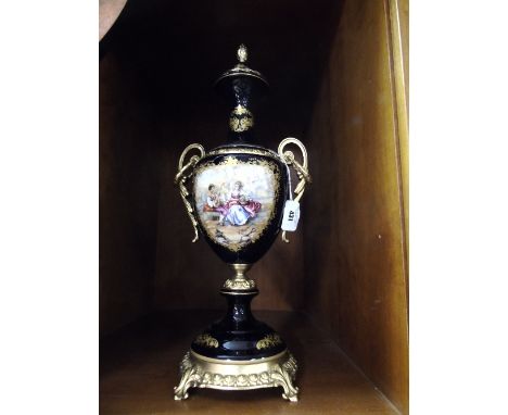 A Cobalt Blue and Gilt Decorated Twin Handled Urn and Lid with central panel depicting a courting couple and pineapple finial