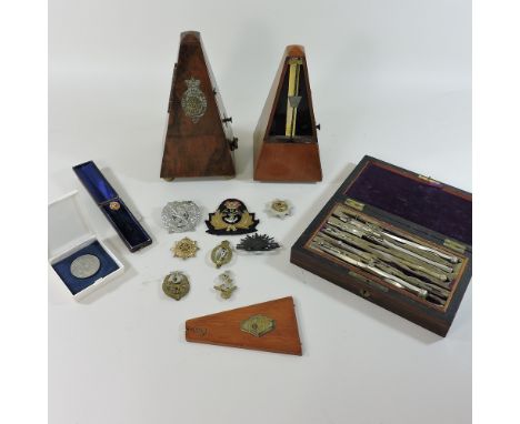 A collection of items, to include two metronomes, a compass set, a Victorian stick pin and military badges