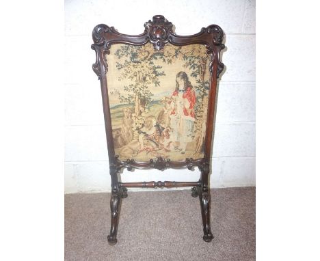 A Victorian mahogany framed firescreen, with an central embroidered panel within carved supports and with leaf capped scroll 