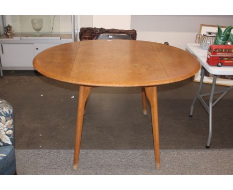 A light Ercol style drop leaf kitchen table, raised on rounded supports