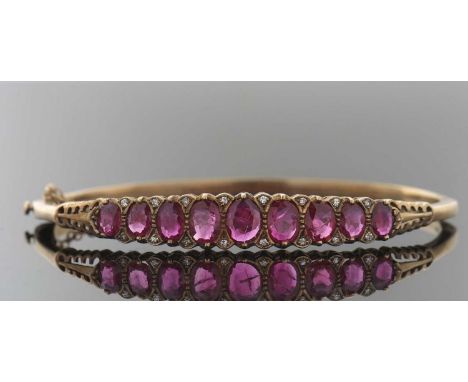 A Victorian style 9ct ruby and diamond hinged bangle, the upper half set with nine graudated oval rubies, interspaced with si