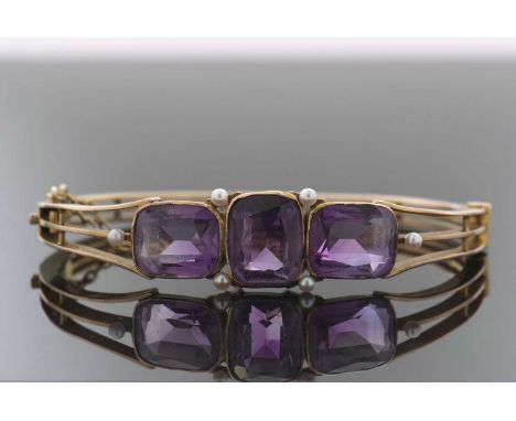 A late 19th century amethyst and seed pearl bangle, set with three rectangular amethysts in collet mounts, the central amethy