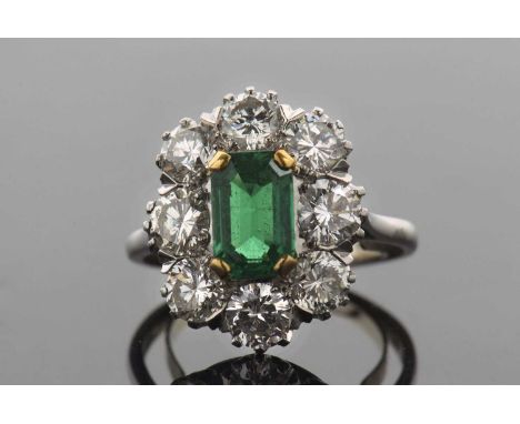 An emerald and diamond cluster ring, the central claw mounted emerald cut emerald, approx. 8.4 x 5.5 x 3.5mm, surrounded by o