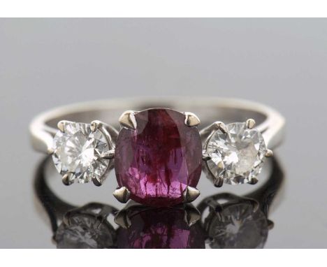 An 18ct white gold ruby and diamond ring, the central off-round ruby in a four claw mount, set to either side with a round br