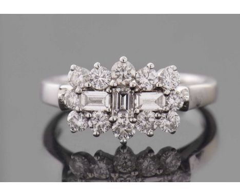 A diamond cluster ring, set with three baguette step cut diamonds to centre and surrounde by round brilliant cut diamonds, to