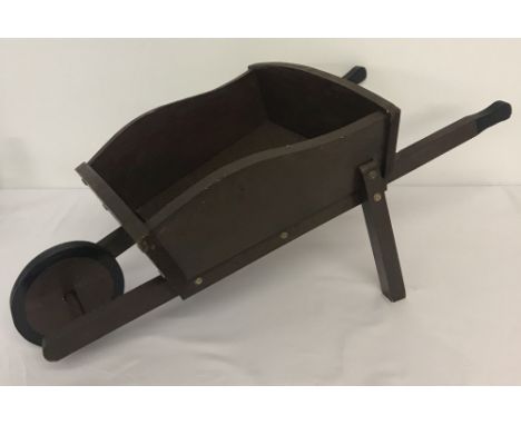 A small vintage handmade wooden wheelbarrow painted brown.