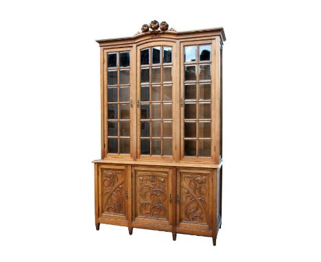 A large Art Nouveau oak library bookcase with three glazed doors, each with bevelled glass panels enclosing a shelved interio
