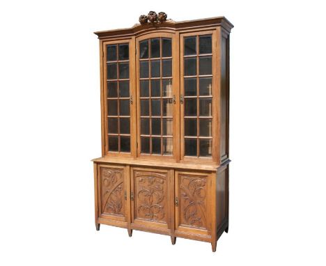 A large Art Nouveau oak library bookcase with three glazed doors, each with bevelled glass panels enclosing a shelved interio