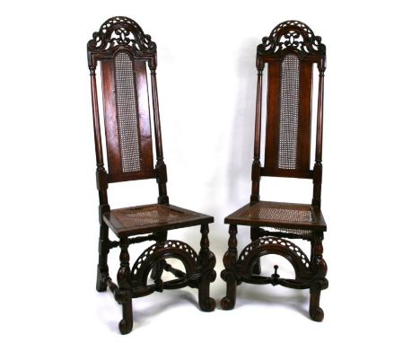 A pair of 17th century style walnut high back dining chairs with carved crest back rails, cane work back panel and seats, on 