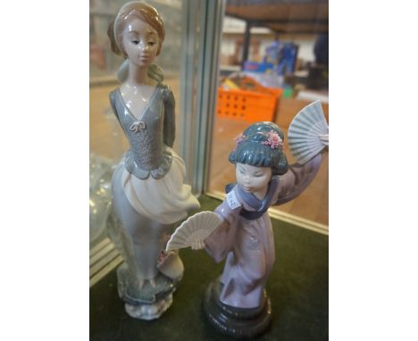 A Lladro figurine of a girl holding a book, together with a further Lladro figure of a lady holding a fan (2)