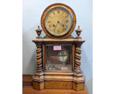 An early 20th century mantel clock with a Roman dial, with a pendulum and key, in a partially glazed display with two barley 