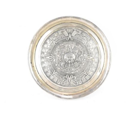 A South American white metal dish having a raised edge and embossed decoration bearing the Aztec calendar, 22cm diameter, 161