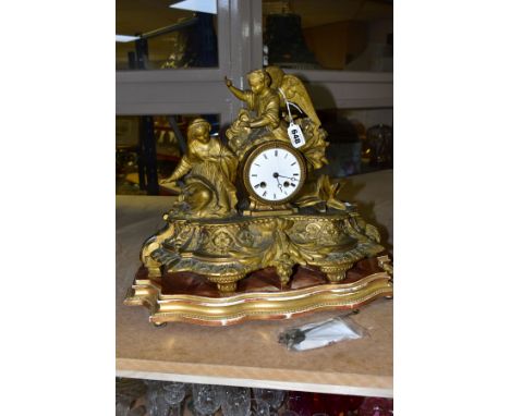 A GILT FIGURAL MANTEL CLOCK, featuring a female kneeling figure and an angel, surrounded by foliate decoration, the white ena