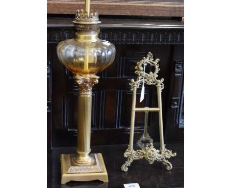 An oil lamp, converted for electricity; a brass Rococo style book stand (2)