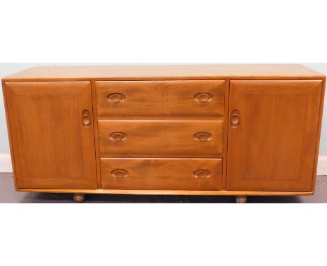 A light elm Ercol low sideboard, with three central drawers flanked by two doors on castors, 115cm wide