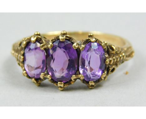 A dress ring, set with three oval cut purple stones, with shaped shoulders, yellow metal, unmarked, 4.6g all in. 