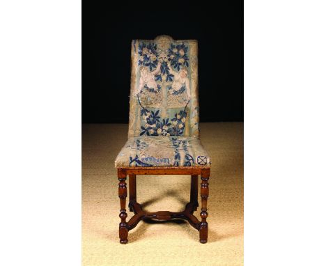 A 17th Century French Upholstered Walnut Side Chair. The break hump top back and seat covered in tapestry fragments and raise