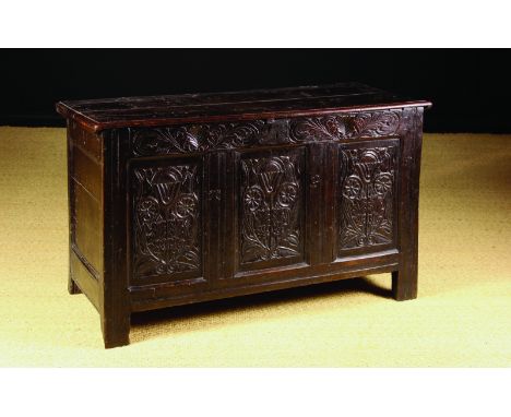 A 17th Century Joined Oak Coffer. The planked top with moulded edge. The triple panel front emblazoned with flowering plants 