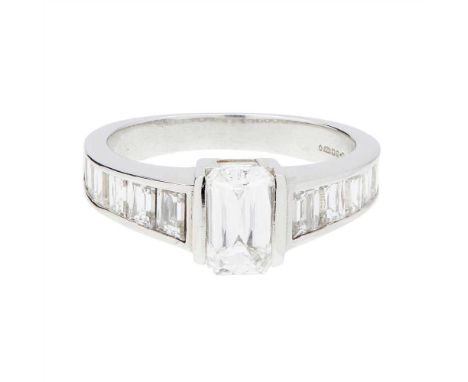 A single stone diamond ring claw set with an emerald cut diamond, each shoulder channel set with tapered scissor/baguette cut