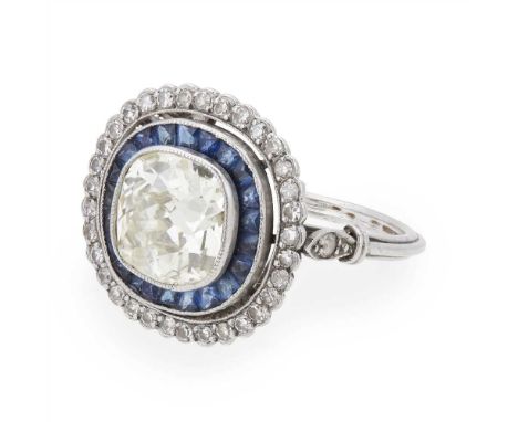 An early 20th century diamond and sapphire set cluster ring millegrain set with a cushion cut diamond in a border of channel 