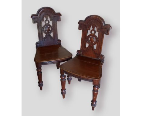 A pair of Victorian hall chairs, each with a shaped pierced back above a panel seat raised upon turned legs 