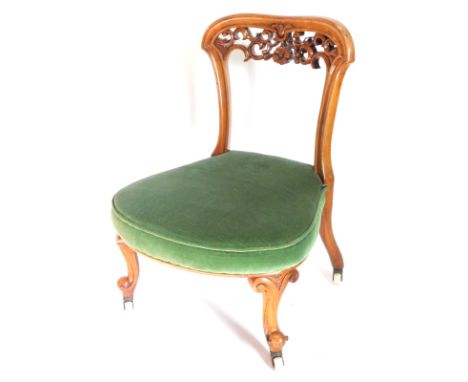 A Victorian walnut nursing chair, with a shaped and pierced back, a green velvet padded seat on short cabriole legs with cera