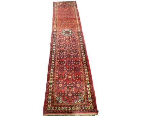 A Persian runner, with an all over geometric design on a red ground with various narrow borders, 77cm x 323cm.
