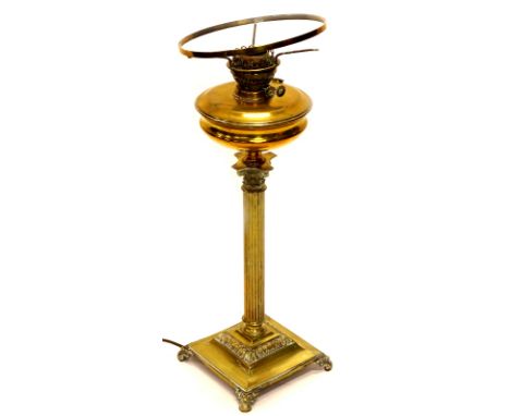 An early 20thC brass oil lamp, with wide circular reservoir on a reeded stem and stepped foot, terminating in scroll feet wit