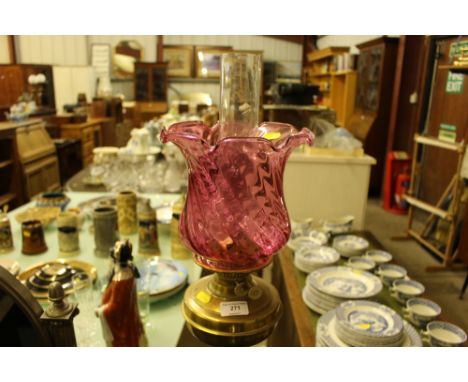 A brass Corinthian column oil lamp with cranberry glass shade