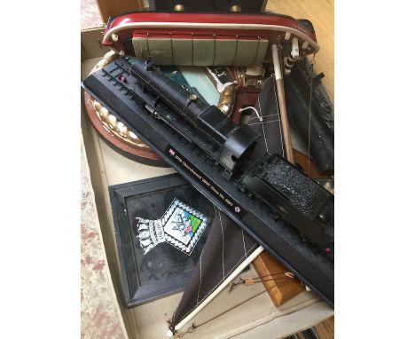 A box of misc comprising four shipping crests, coal model of the Titanic, model tank engine and a wooden model sailing boat. 