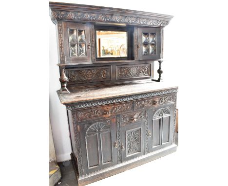 AN EDWARDIAN OAK DRESSER  the upper section with carved frieze above mirror flanked by cushion shaped glazed doors, the base 