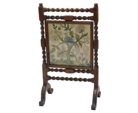 A late 19thC/early 20thC oak fire screen, with spirally turned supports, surrounding a central grill work panel, depicting an