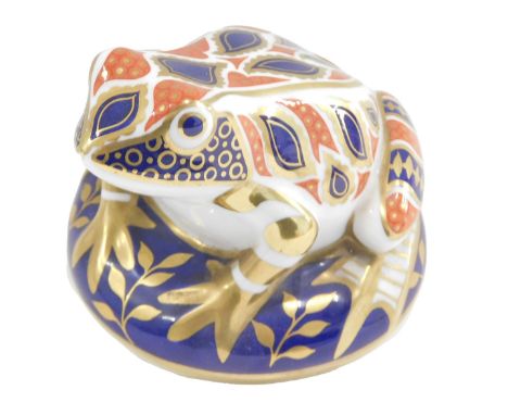  A Royal Crown Derby porcelain frog paperweight, on a circular base, printed mark in red to underside, gold button, 9cm wide.