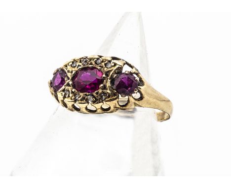 An Edwardian ruby and diamond dress ring,  the three mixed cut rubies, in an oval shaped setting surrounded by diamond chips,