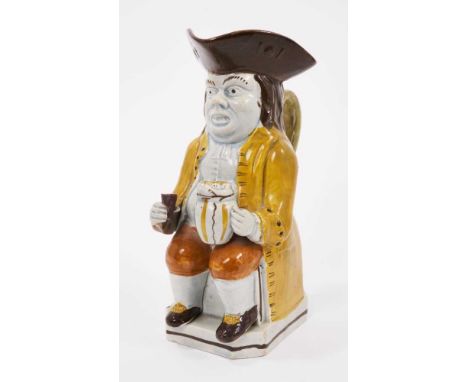 Prattware Toby jug, circa 1800, shown seated, with glass of beer in one hand and a foaming tankard in the other, wearing a ye