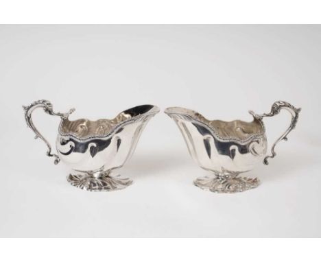 Pair of late Victorian silver sauce boats of shell form with gadrooned borders, and leaf mounted scroll handles, on stylized 