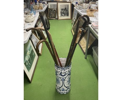 A BLUE AND WHITE CERAMIC STICK STAND, SLIGHTLY A/F TO INCLUDE A QUANTITY OF WALKING STICKS 