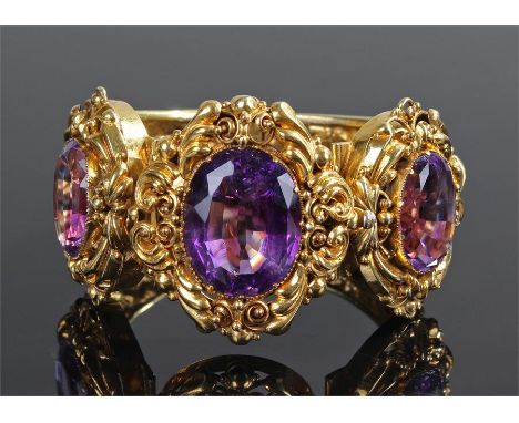 Victorian yellow metal and amethyst bangle, set with three facetted amethyst and foliate scroll mounts, 7.5cm wide