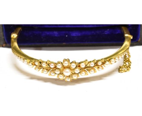 A LATE VICTORIAN GOLD AND HALF-PEARL HINGED KNIFE-EDGE BANGLE the front designed as a flower-head between tapering leaves and