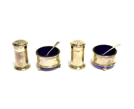 A SILVER FOUR PIECE CRUET SET AND TWO SPOONS Comprising; two round salts on ball feet with blue glass liners and two cylindri