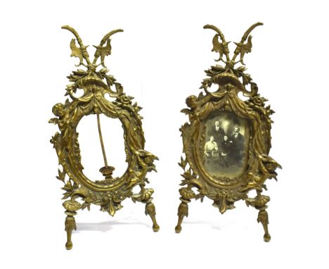 A PAIR OF LATE 19TH CENTURY GILT BRASS EASEL TYPE PHOTOGRAPH FRAMES  in the Rococo style, the oval apertures flanked with var