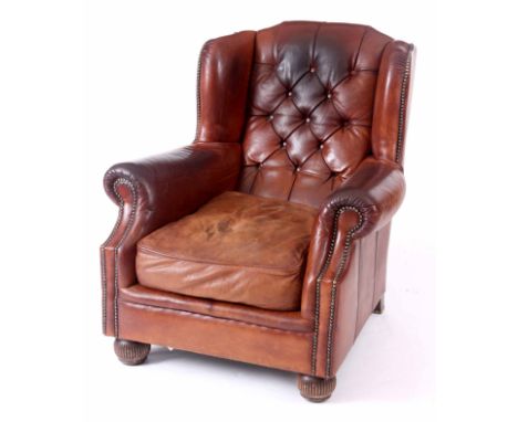 A BROWN TAN LEATHER BUTTON BACKED WINGED ARMCHAIR with stud work and loose cushion seat 104cm high 87cm wide.