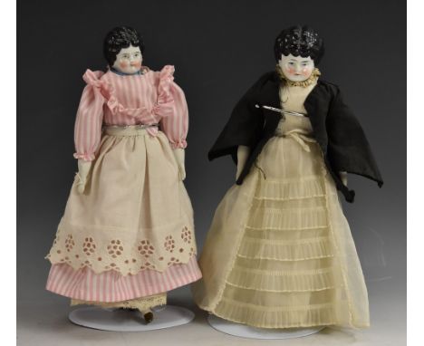 A pair of moulded ceramic head dolls, painted features and black hair, blue eyes, rosy cheeks, stuffed bodies, pottery arms a
